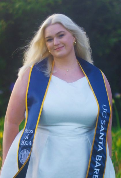 grace carpenter is a young woman with blonde hair. she is wearing a white dress and a graduation sash that reads UC Santa Barbara